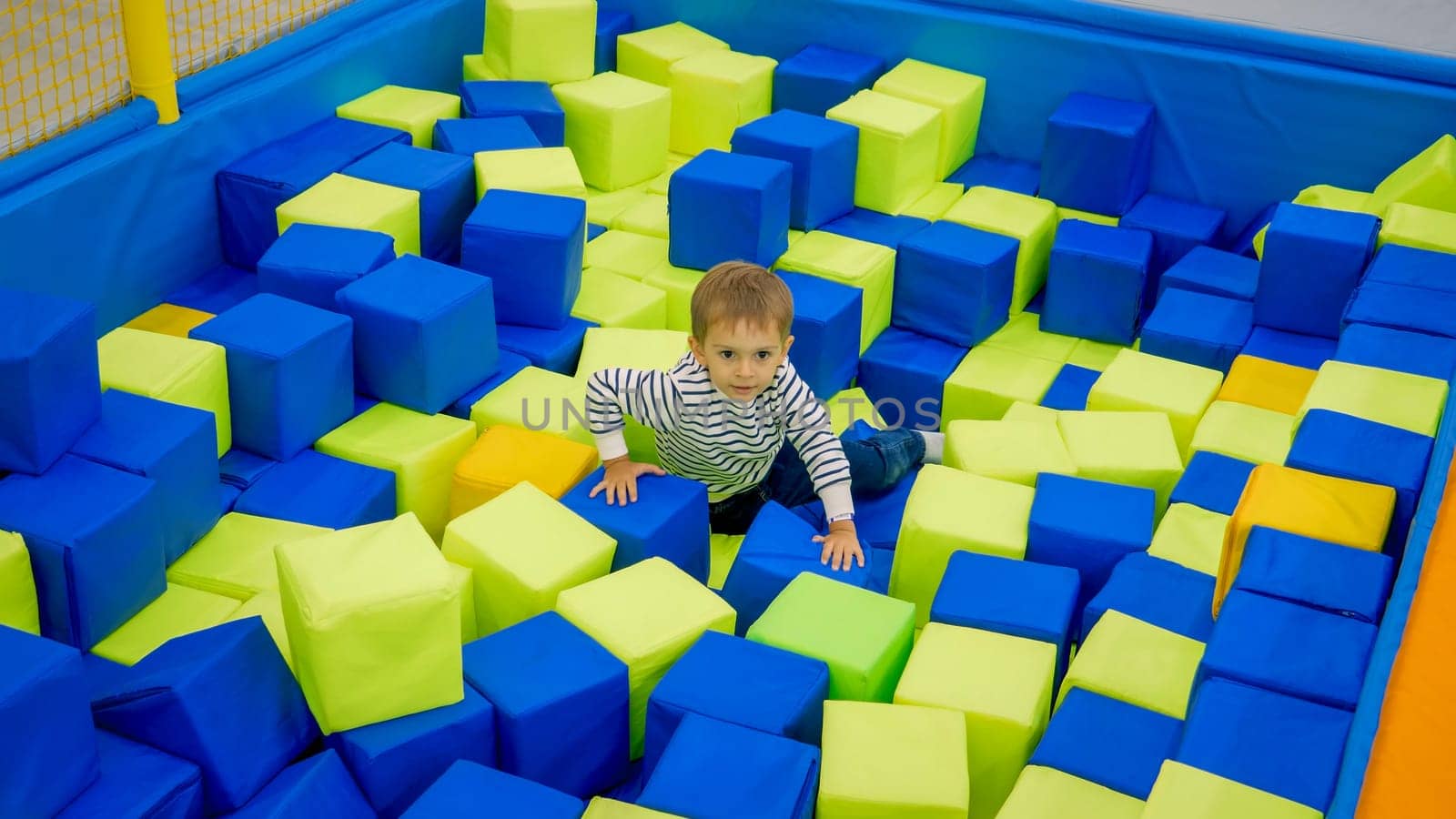 Cute little boy playing in pool full of soft cubes in palyroom.