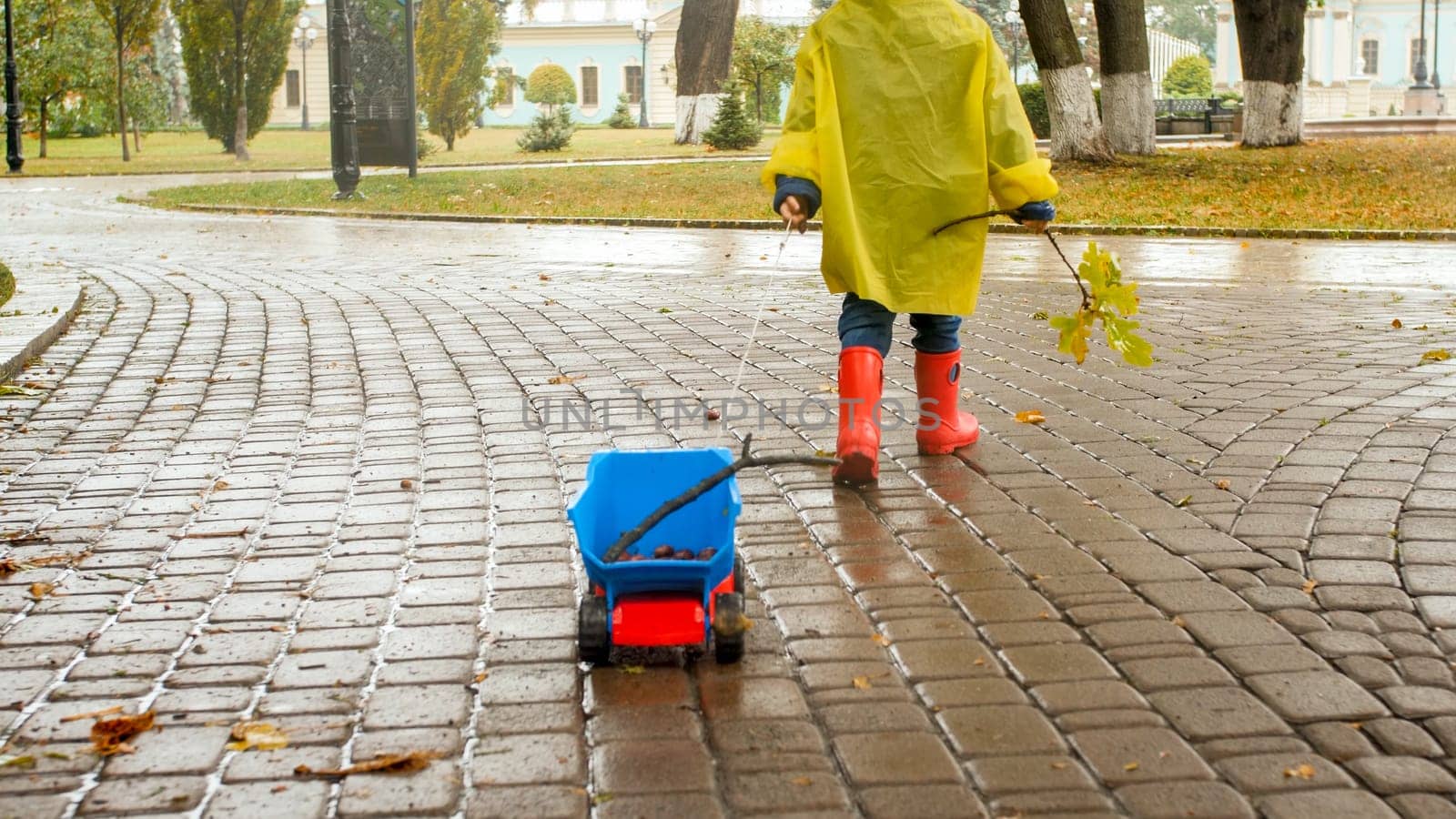 Closeup photo of little boy pulling hif toy truck in park on rainy autumn day.