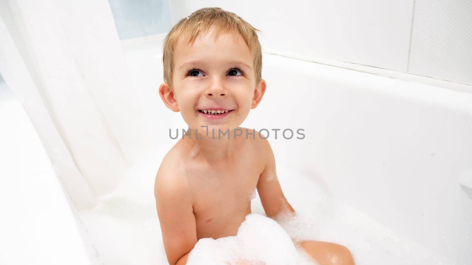 Portrait of happy smiling little boy enjoying bathing with soap foam.