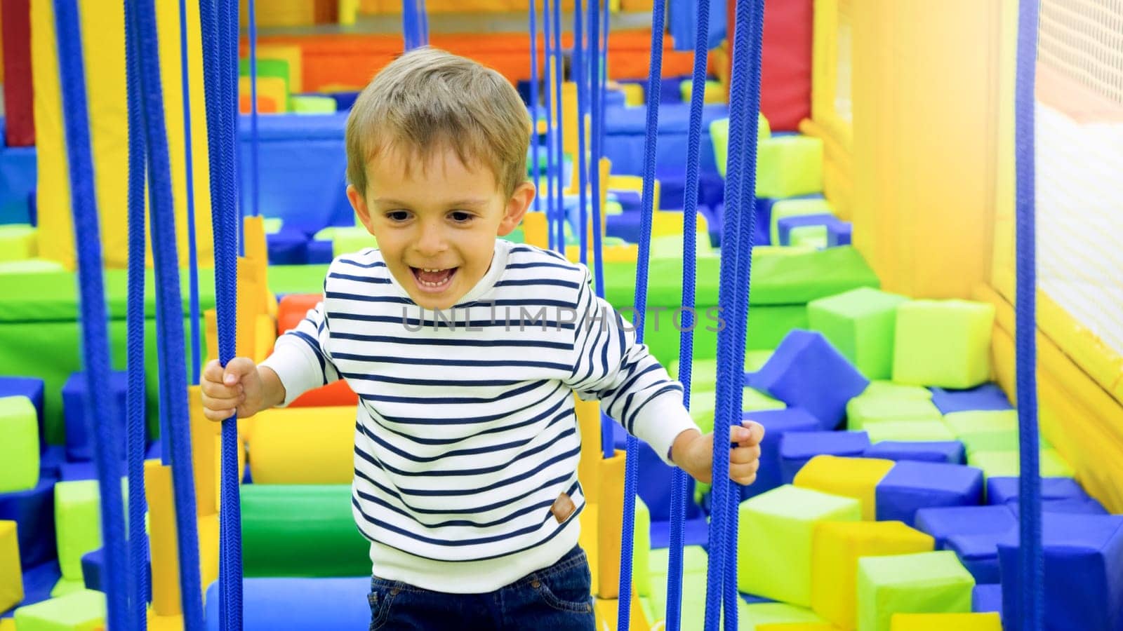 Portrait of happy smiling boy playing and climbing on ropes on the playground at amusement park.