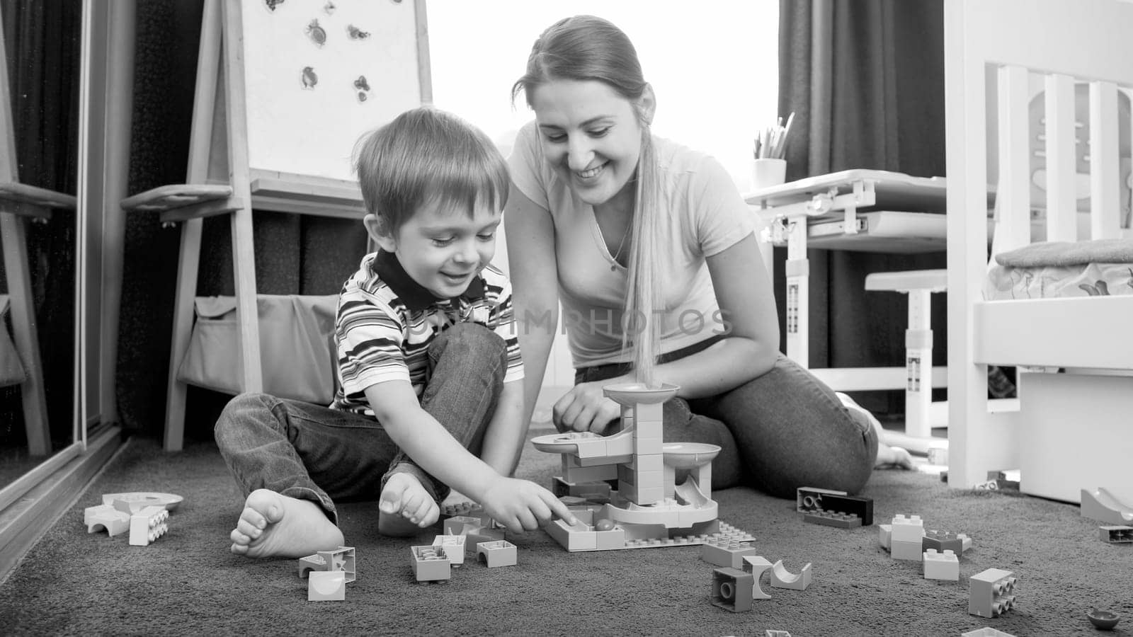 Happy little boy with mother building toy track with blocks and bricks.