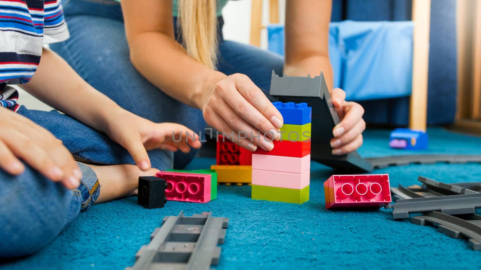 Closeup image of mother and son assembling toy bridge from colorful constructor bricks and blocks.