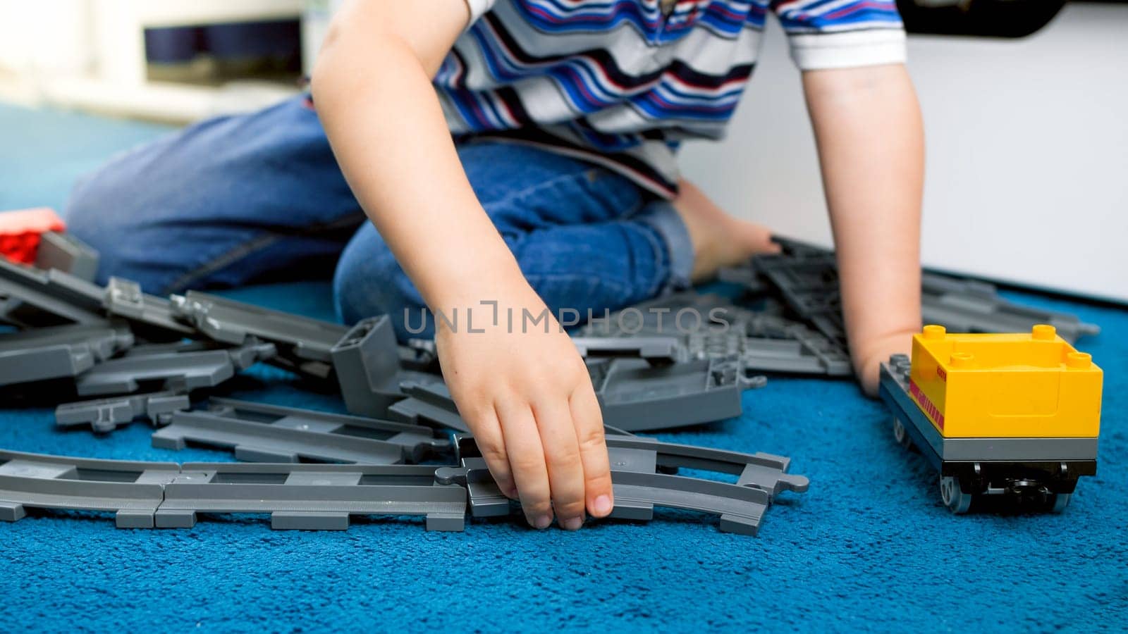 Closeup image of child's hand assembling toy railroad on floor.