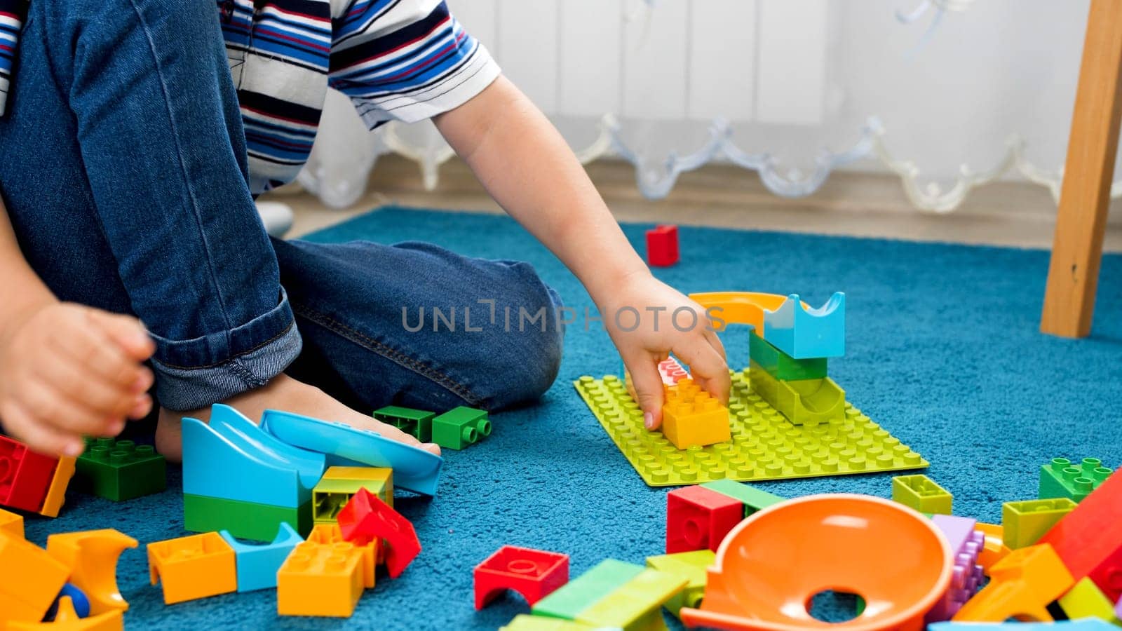 Closeup image of little boy assembling colorful toy constructor on carpet.