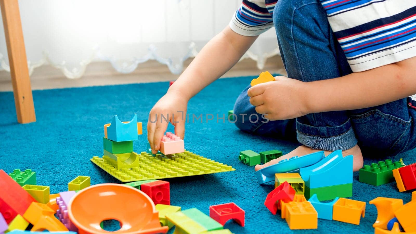 Closeup image of little boy sitting on floor and playing with toy blocks.