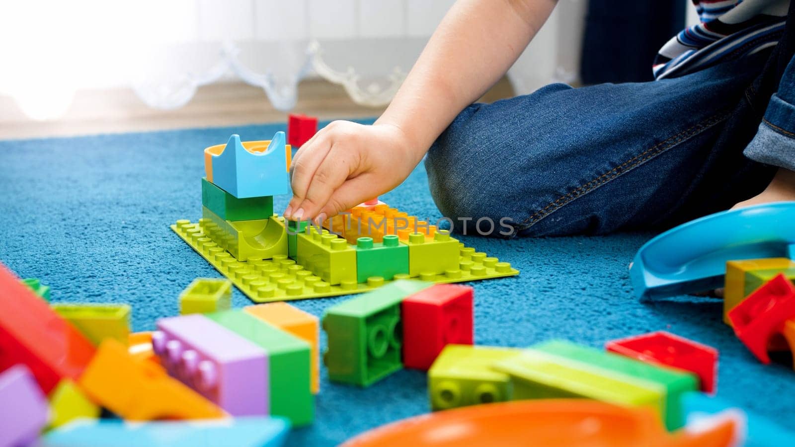 Closeup photo of child hand assemblind toy constructor and building a house.