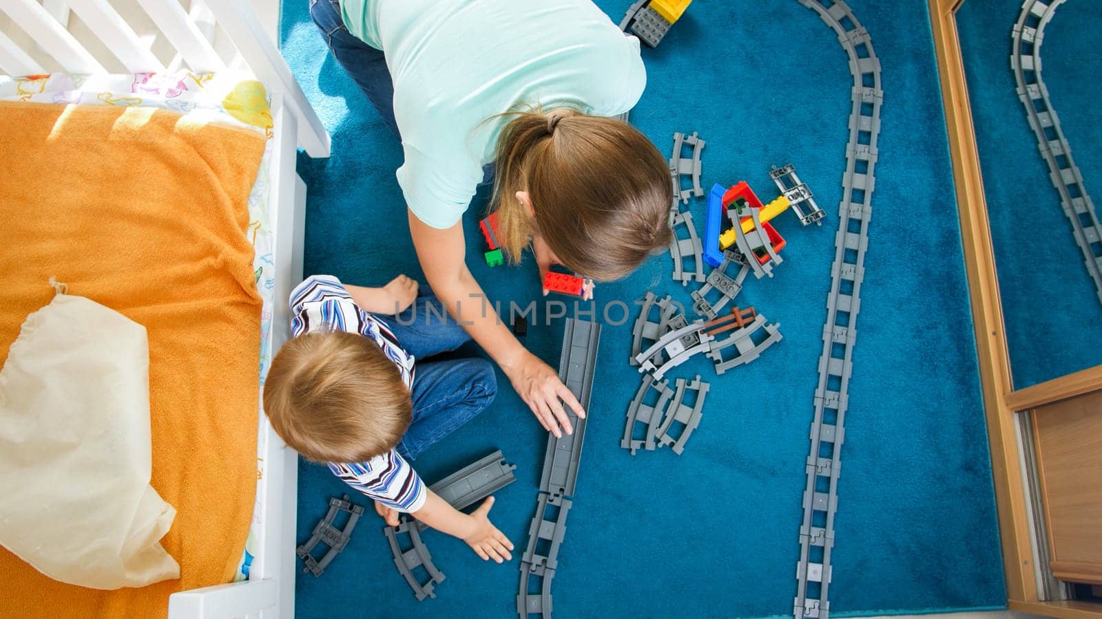View from the top on litttle boy with mother building and playing with toy railroad and train.