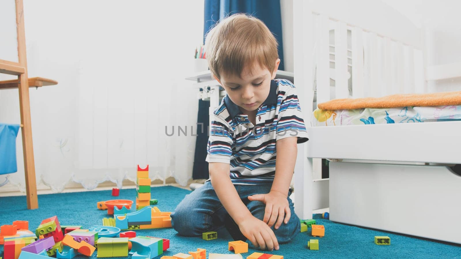 Toned photo of little smiling boy playing with constructor blocks in his bedroom.