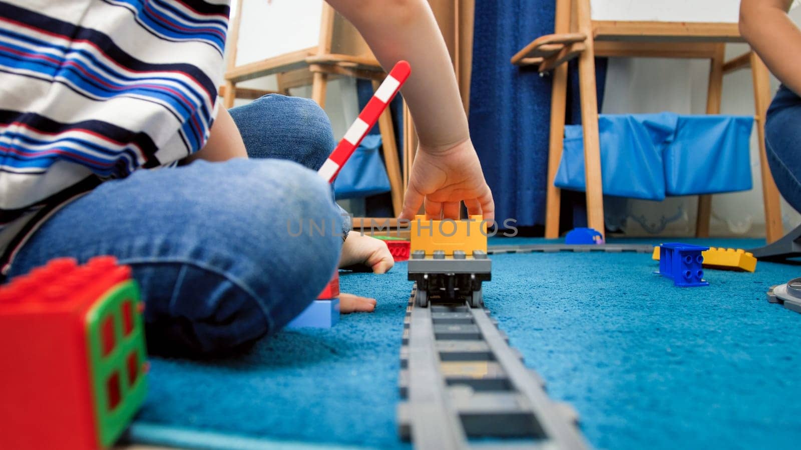 Little 4 years old boy sitting on carpet and playing with toy trains.