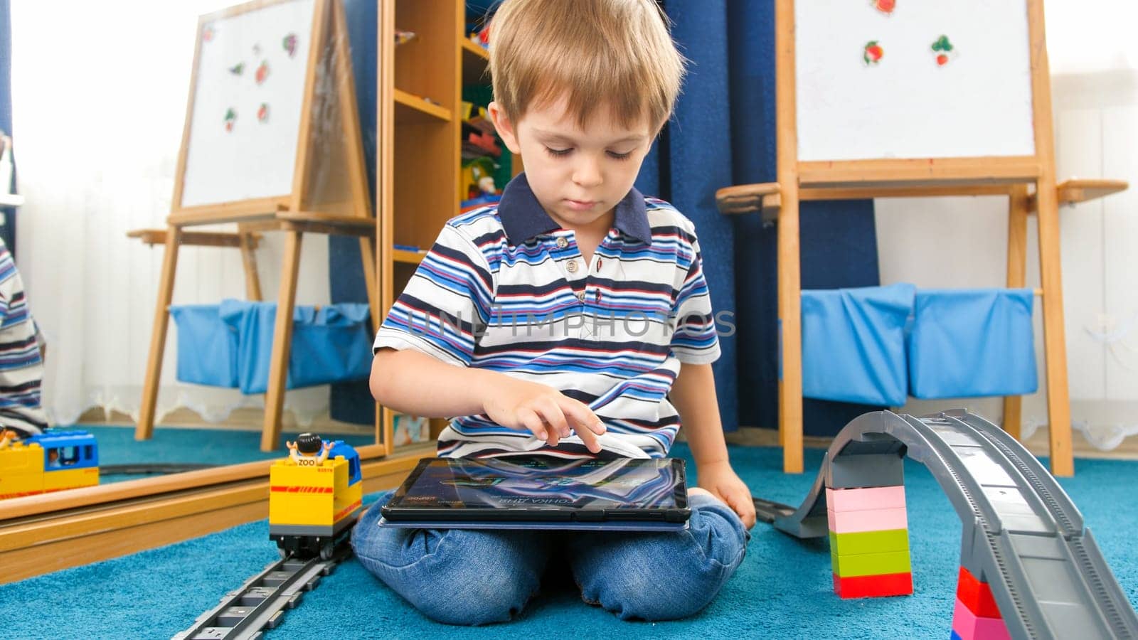 Little boy sitting on floor at home and playing games on tablet computer.