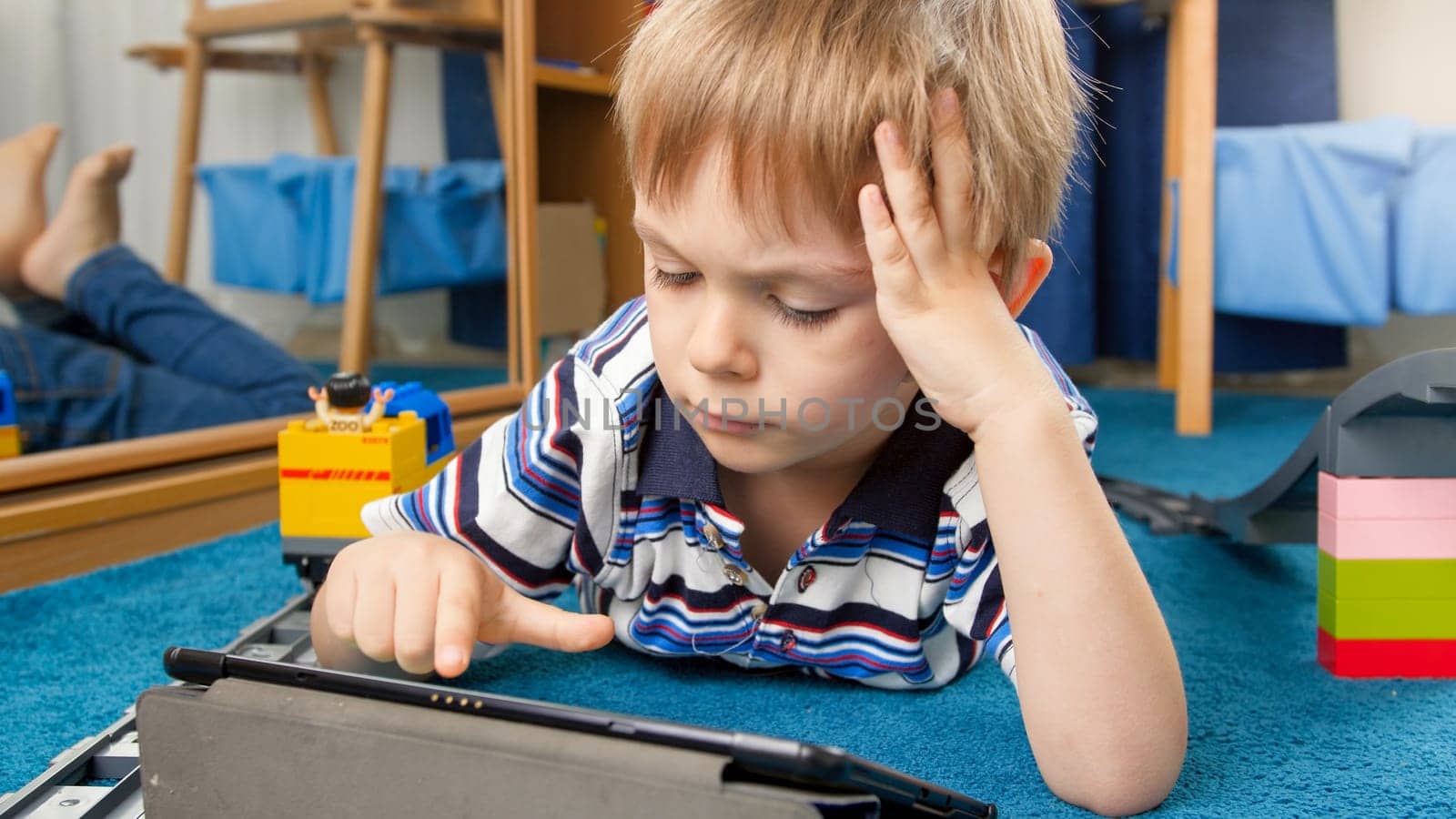 Portrait of concentrated little boy using tablet computer.