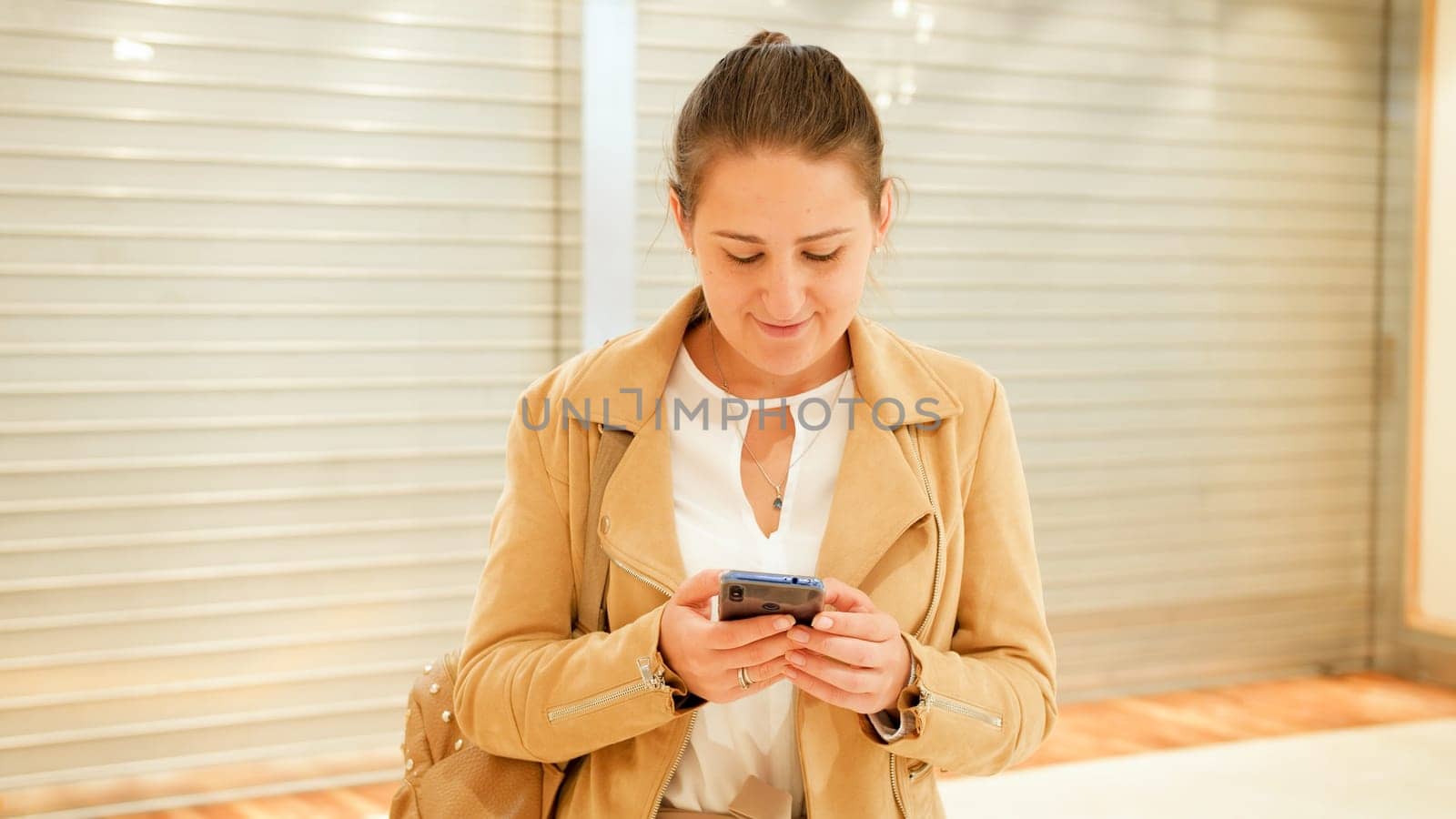 Portrait of young stylish woman typing message on smartphone at shopping mall.