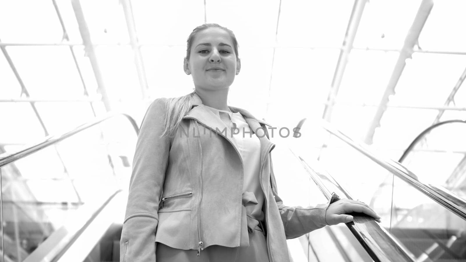 Black and white portrait of beautiful young woman standing on escalator in shopping mall.