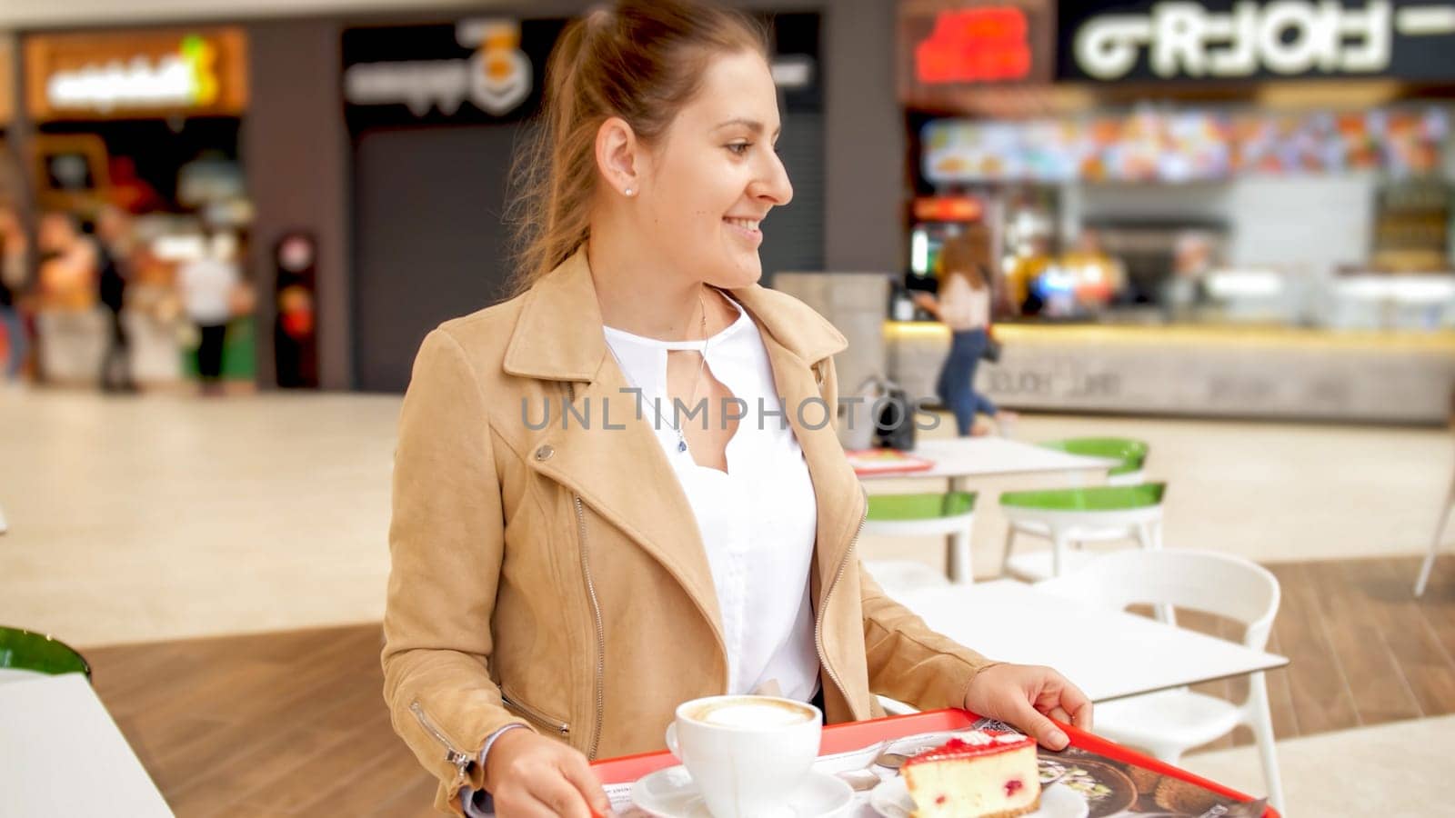 Portrait of smiling young woman holding food tray searching for free place in cafe.