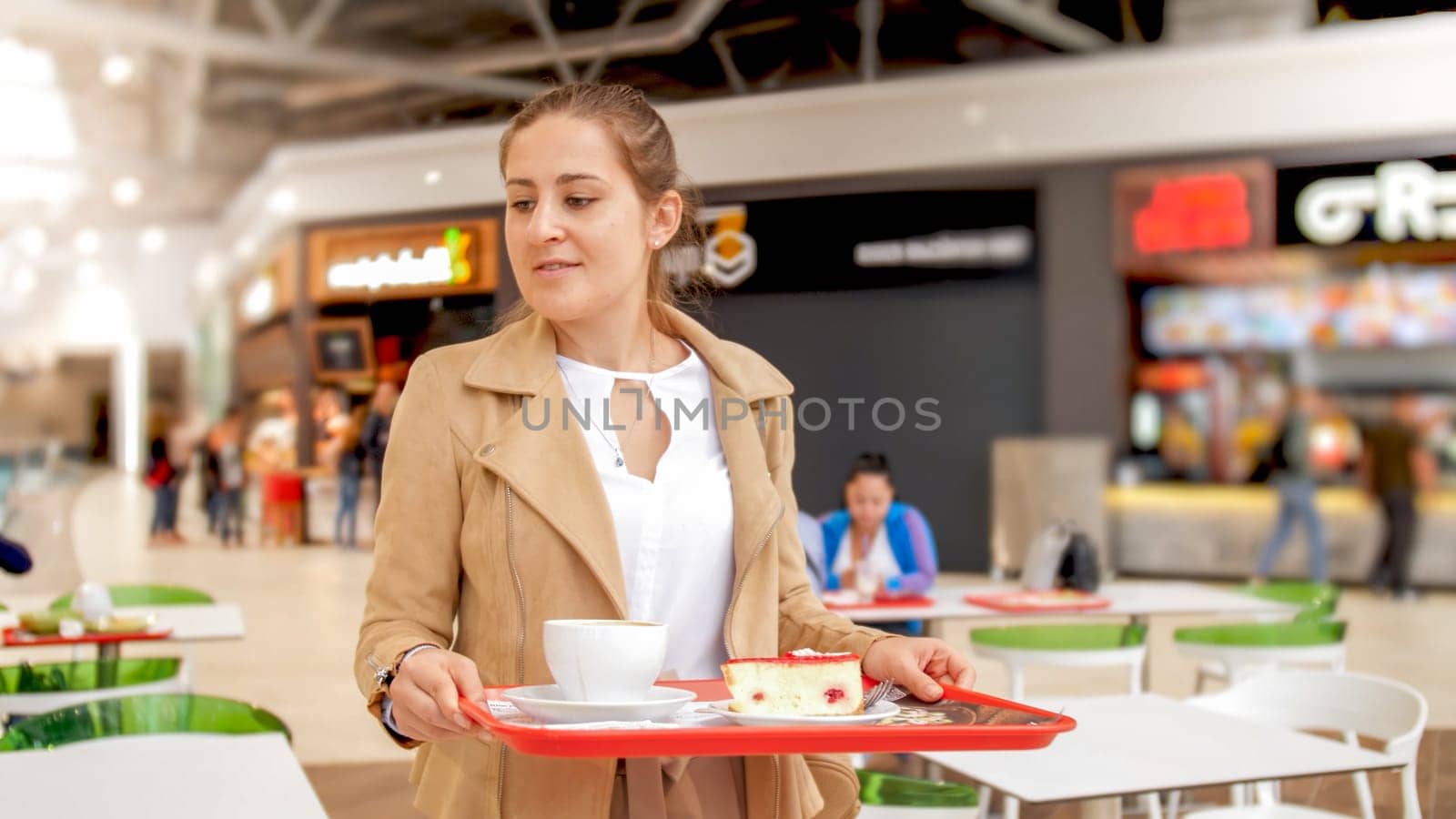 Portrait of young girl holding food on tray looking for place to eat on food court at shopping mall.