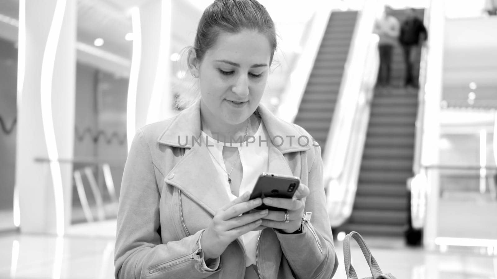 Black and white portrait of beautiful young woman in shopping mall browsing internet on smartphone.