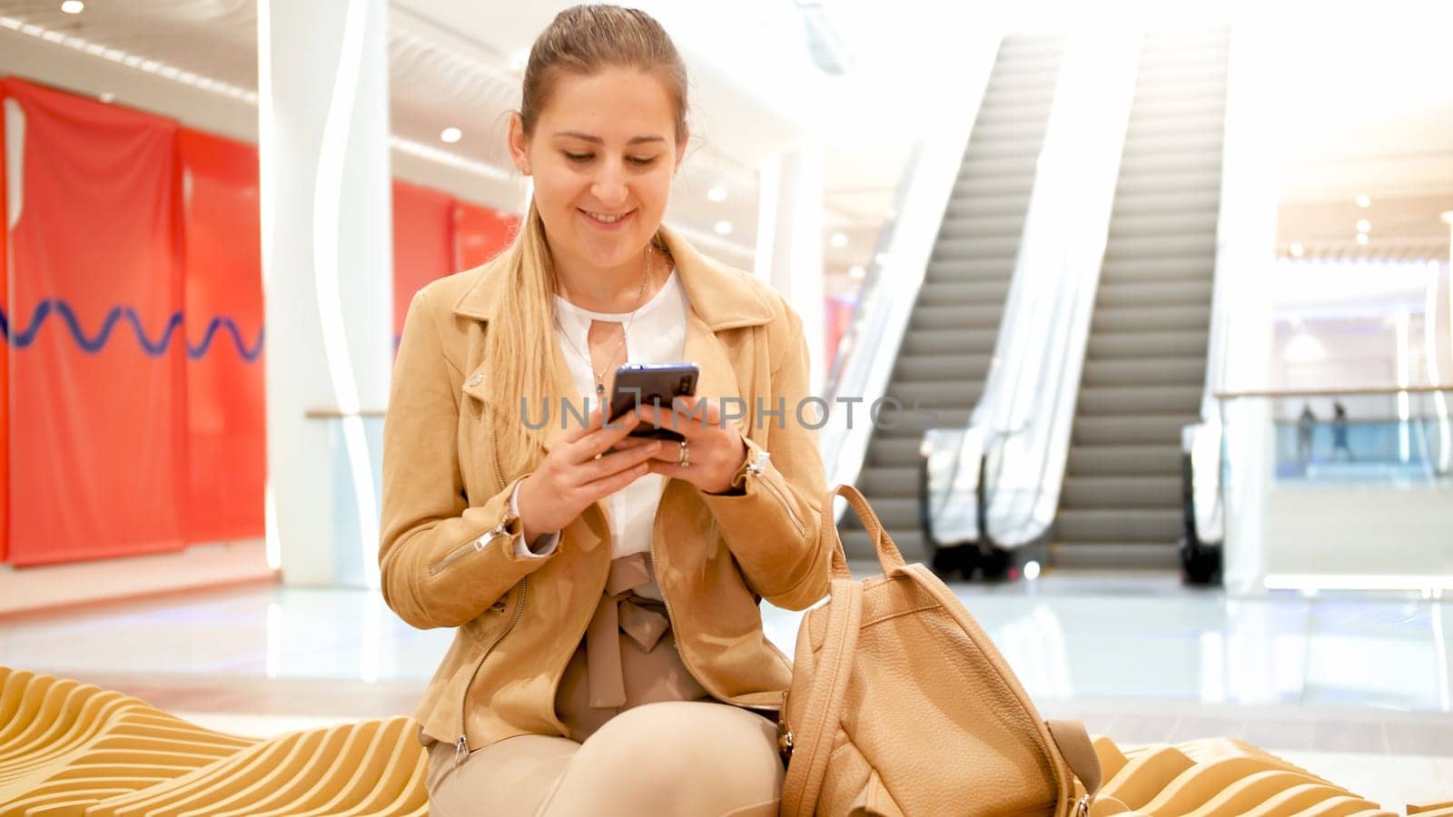 Portrait of beautfiul young woman sitting in shopping mall and using smartphone.