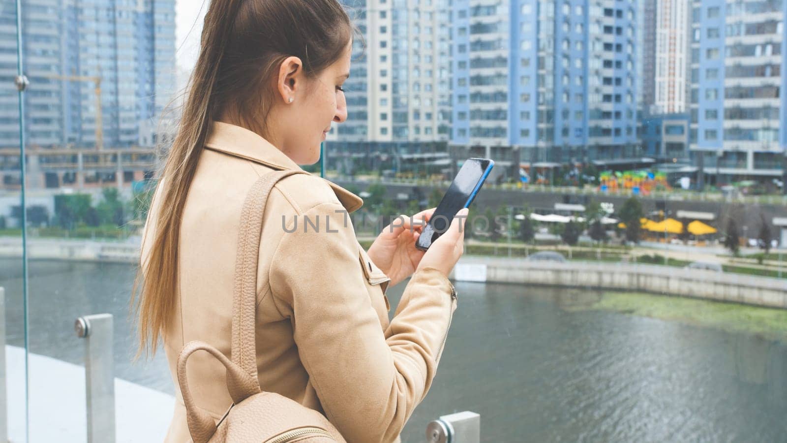 Toned portrait of young woman standing on building top and using smartphone.