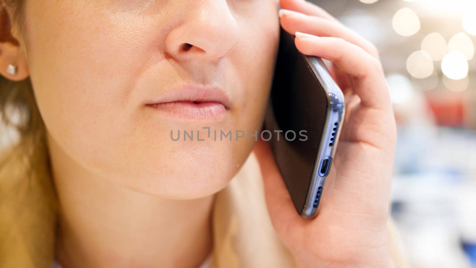 Closeup image of female mouth talkin by phone in cafe.