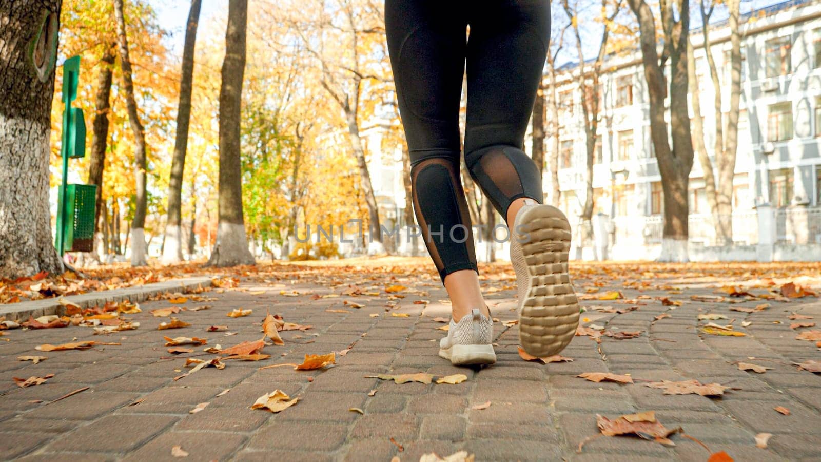 Closeup photo of female feet in sneakers jogging in autumn park.