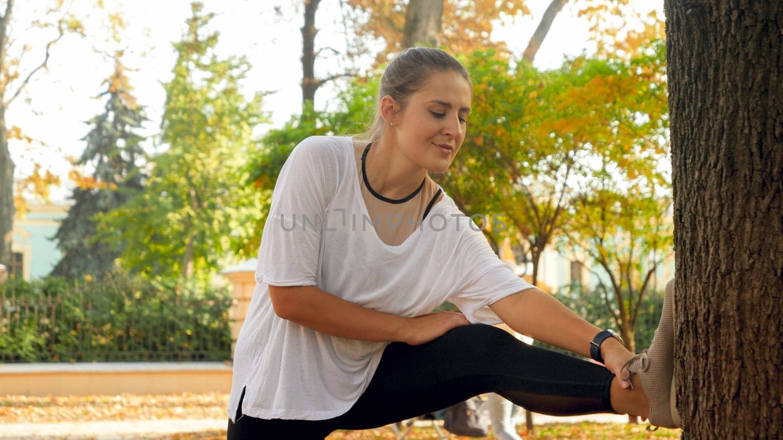 Portrait of beautiful smiling woman stretching and warming up before doing fitness exercises in autumn park.