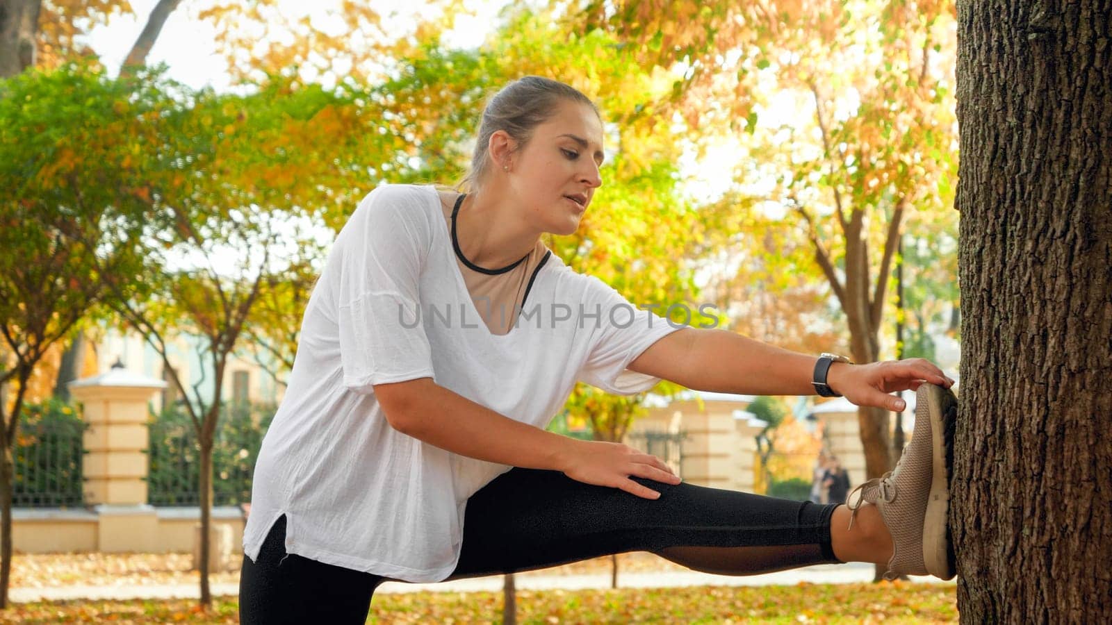 Portrait of sporty young woman stretching her muscles before doing sports exercises in autumn park.