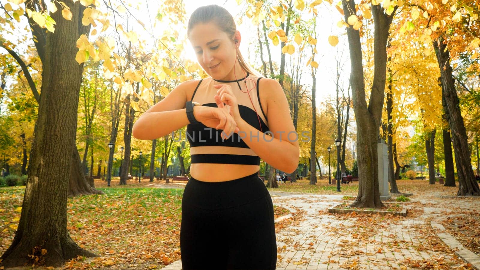Portrait of smiling sporty woman using smartwatch or fitness tracker during sport exercises in autumn park.