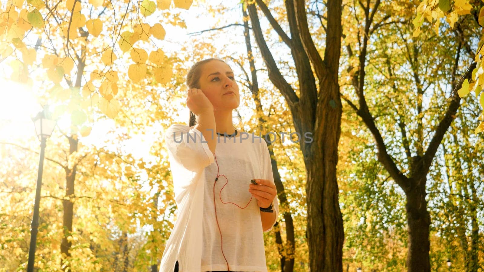Portrait of beautiful young woman putting on headphones with music before jogging at autumn park.
