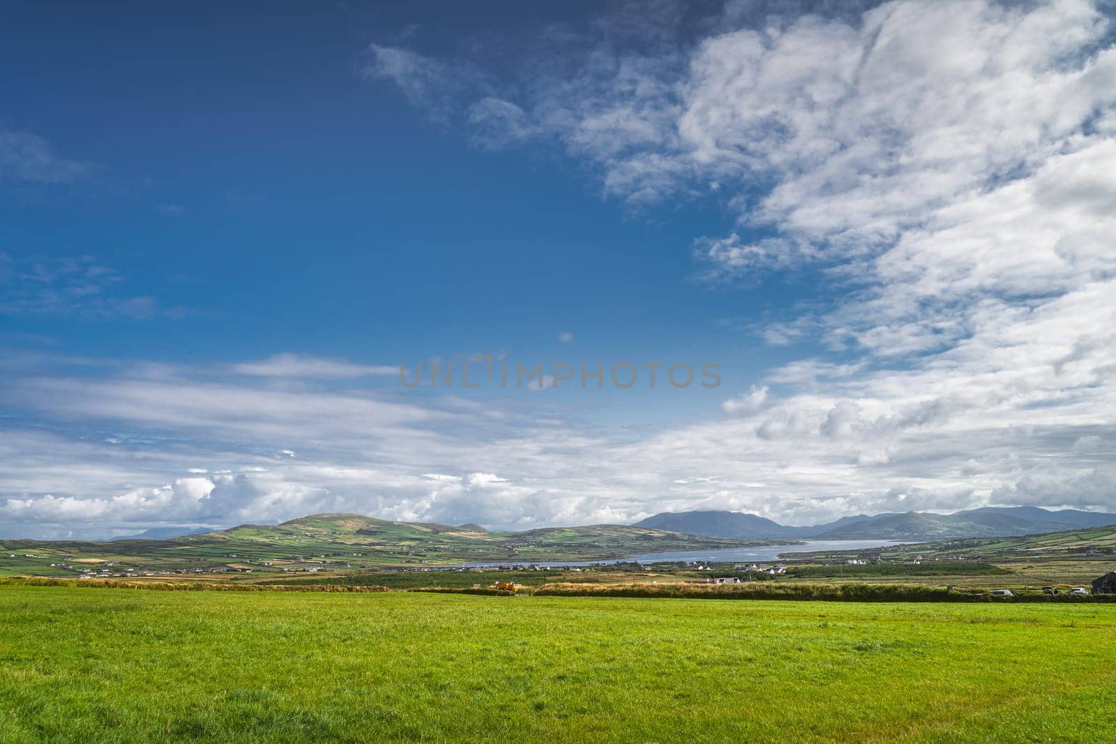 View from Kerry Cliffs on green fields or pasture, mountains and Portmagee village in far distance at beautiful sunny day, Ring of Kerry, Ireland