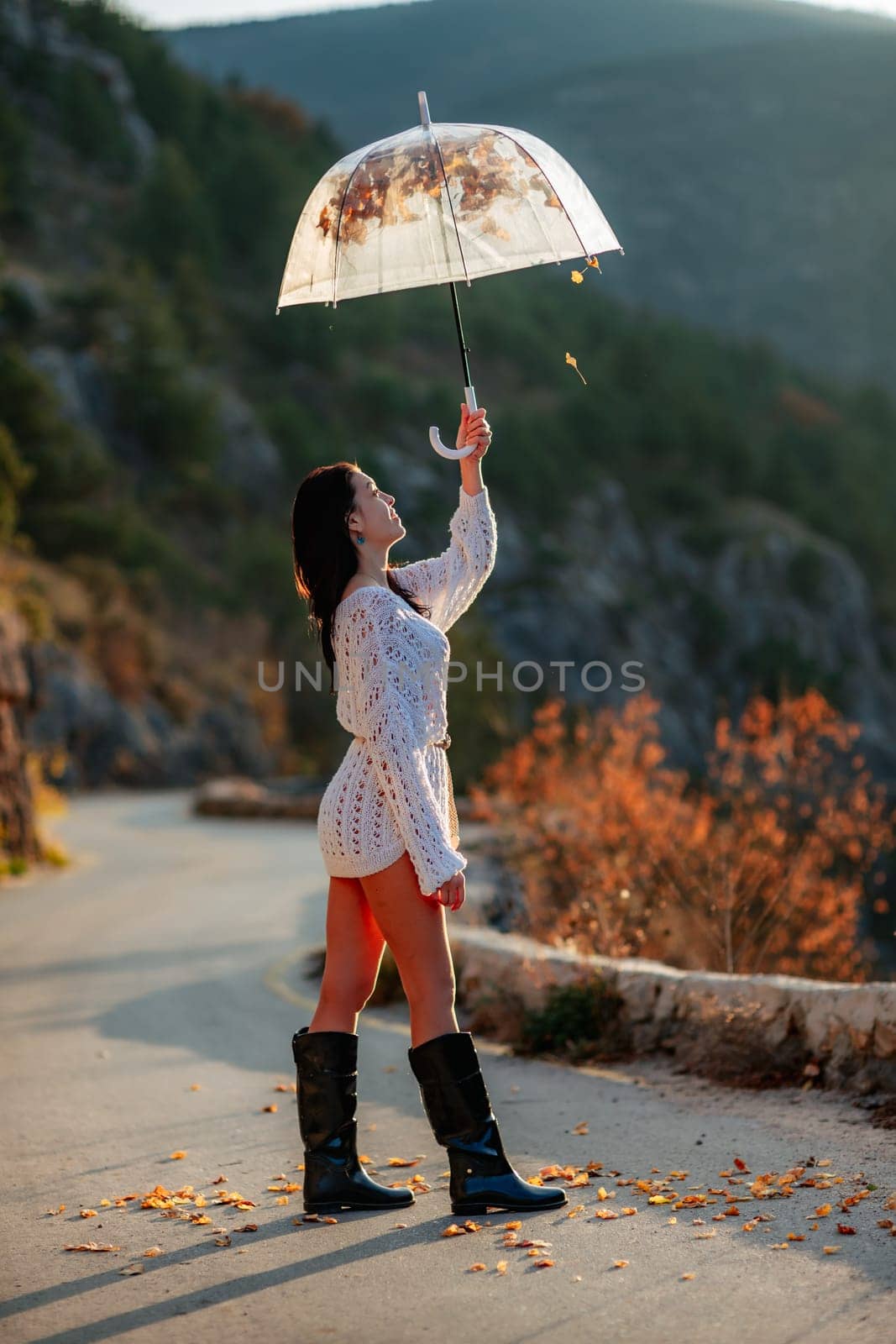 woman umbrella leaves , She holds him over her head, autumn leaves are falling out of him. Beautiful woman in a dress with an umbrella in the autumn park on the road in the mountains