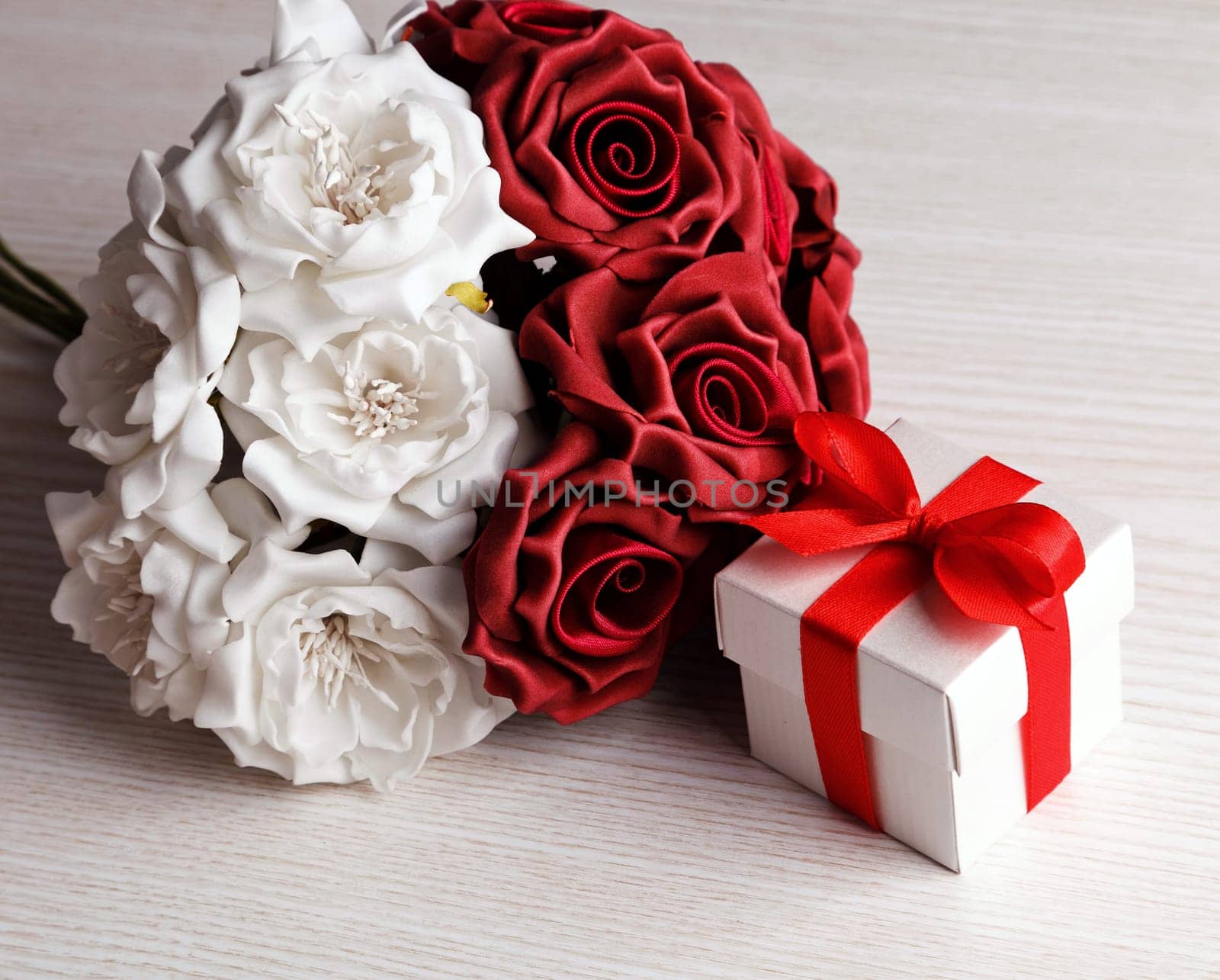 red and white roses and red gift box with yellow ribbon on wooden surface