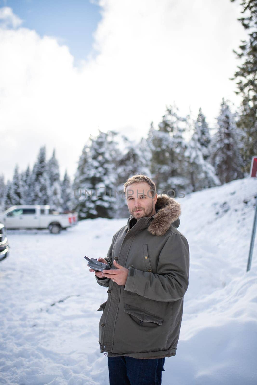 Handsome man holding drone remote control with a beautiful snowy forest as background. Portrait of happy man controlling drone in frozen woods. Adventurous winter holiday