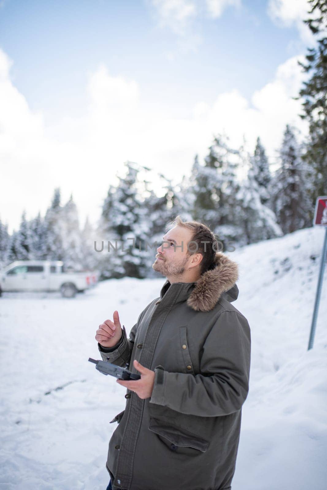 Handsome man holding drone remote control and giving thumps up in beautiful snowy forest. Portrait of happy man controlling drone in frozen woods. Adventurous winter holiday
