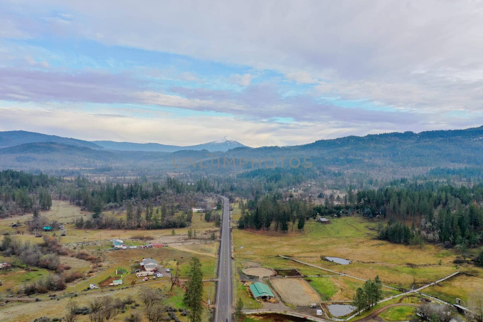 Beautiful and peaceful forest under cloudy sky and with mountains as background. Aerial view of road in the middle of the woods. Wooded and rocky landscapes