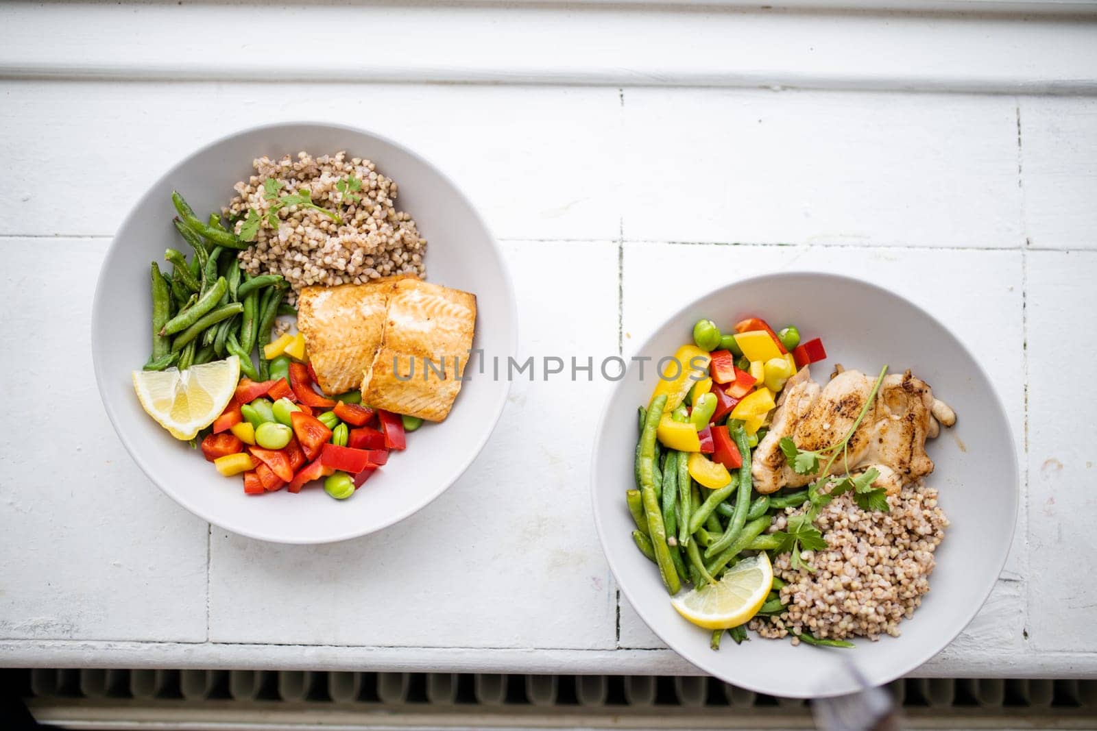 Top view of chicken and salmon dishes with buckwheat, green beans, broad beans, tomato, and pepper slices. Nutritious dishes with vegetables and meat on white plates. Healthy balanced diet