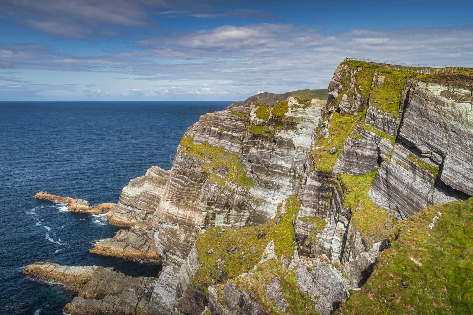 Tourists standing on the top of majestic and beautiful Kerry Cliffs with a view on Atlantic Ocean, sunny summer day, Portmagee, Ring of Kerry, Ireland
