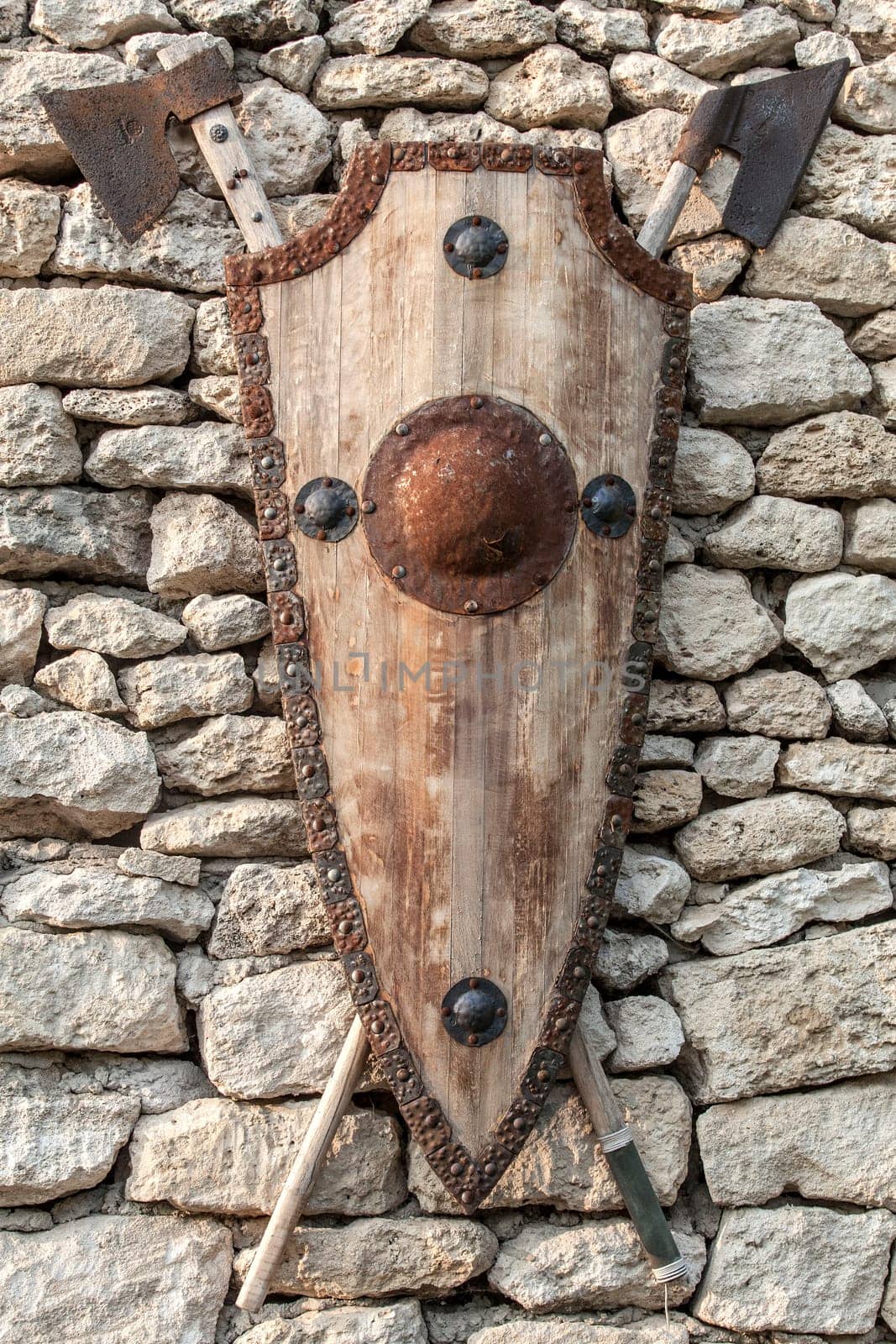 Ancient weapons wall. Wooden shield with iron accents and axes.