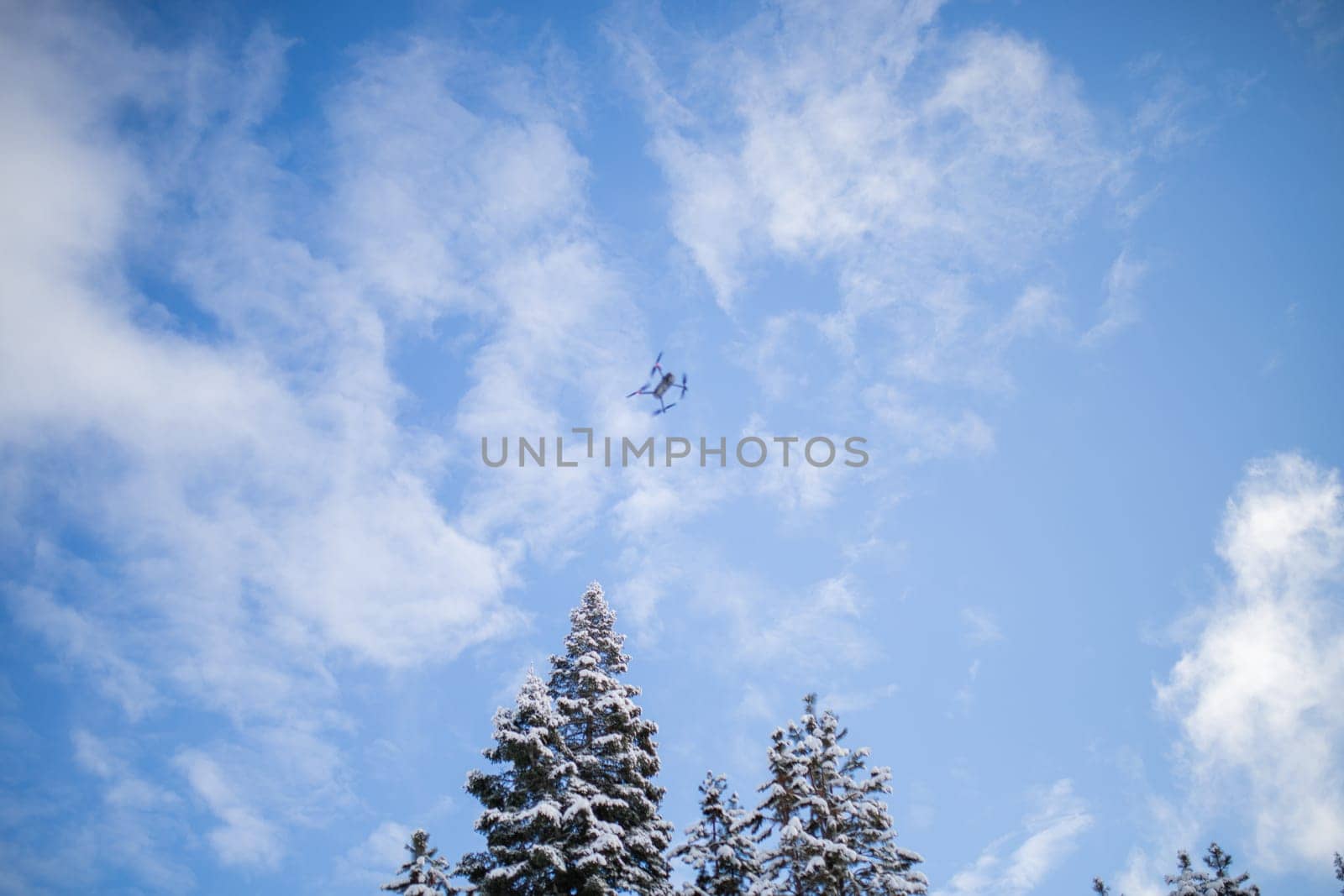 Drone flying over beautiful snowy forest under slightly cloudy blue sky. Drone exploring the calm frozen pine trees. Beautiful winter landscapes