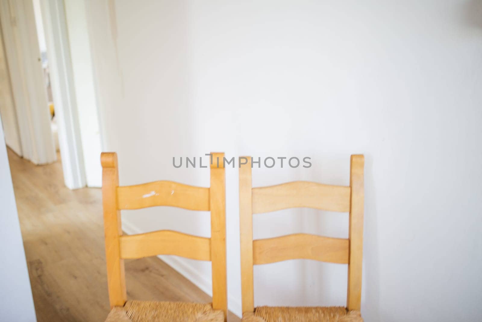 Two wooden chairs on long empty hall with white walls and wooden floor. Brown hairs inside house with white interiors. Minimalistic design furniture