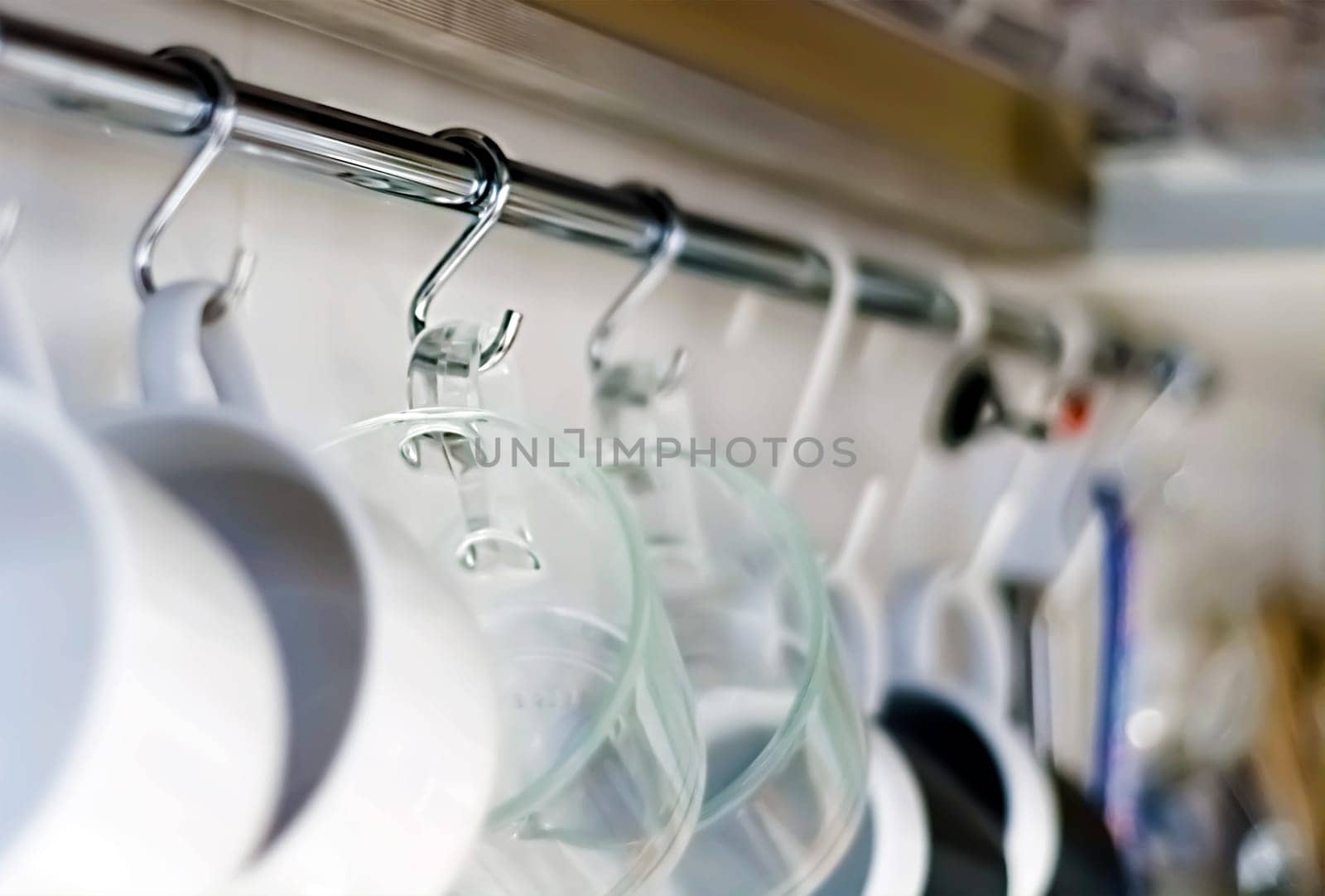 A set of mugs hanging on hooks in a modern home kitchen. Everyday objects. Domestic life.