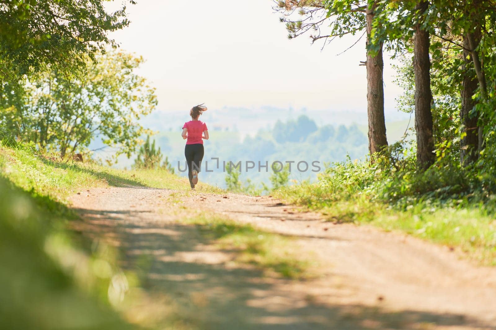 woman enjoying in a healthy lifestyle while jogging on a country road through the beautiful sunny forest, exercise and fitness concept
