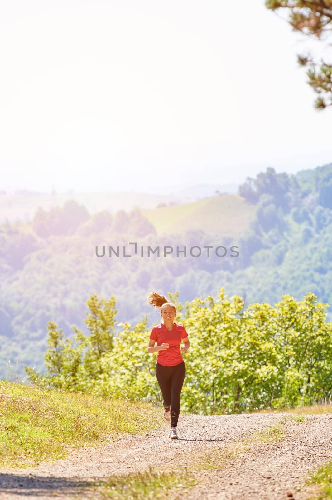 woman enjoying in a healthy lifestyle while jogging on a country road through the beautiful sunny forest, exercise and fitness concept