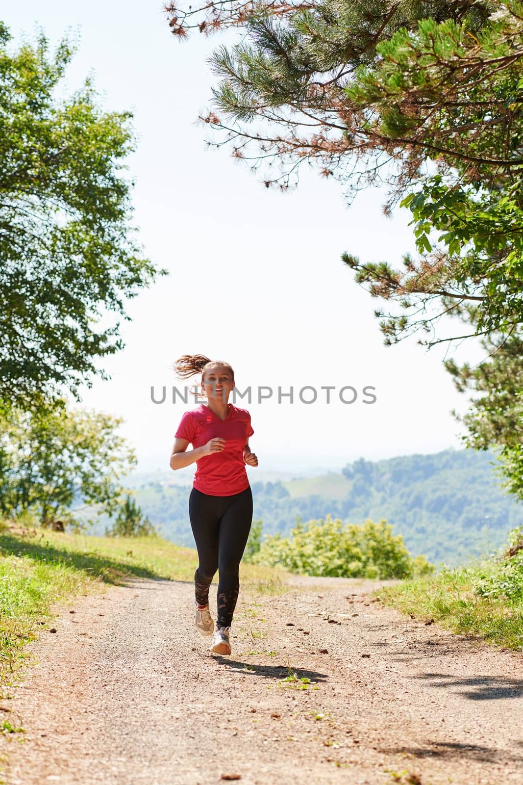 woman enjoying in a healthy lifestyle while jogging on a country road through the beautiful sunny forest, exercise and fitness concept