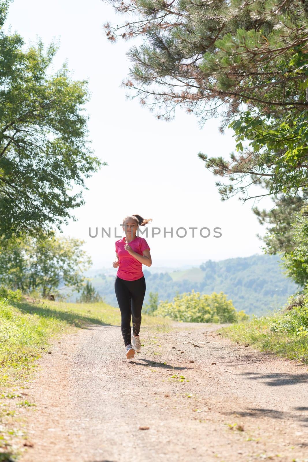 woman enjoying in a healthy lifestyle while jogging on a country road through the beautiful sunny forest, exercise and fitness concept
