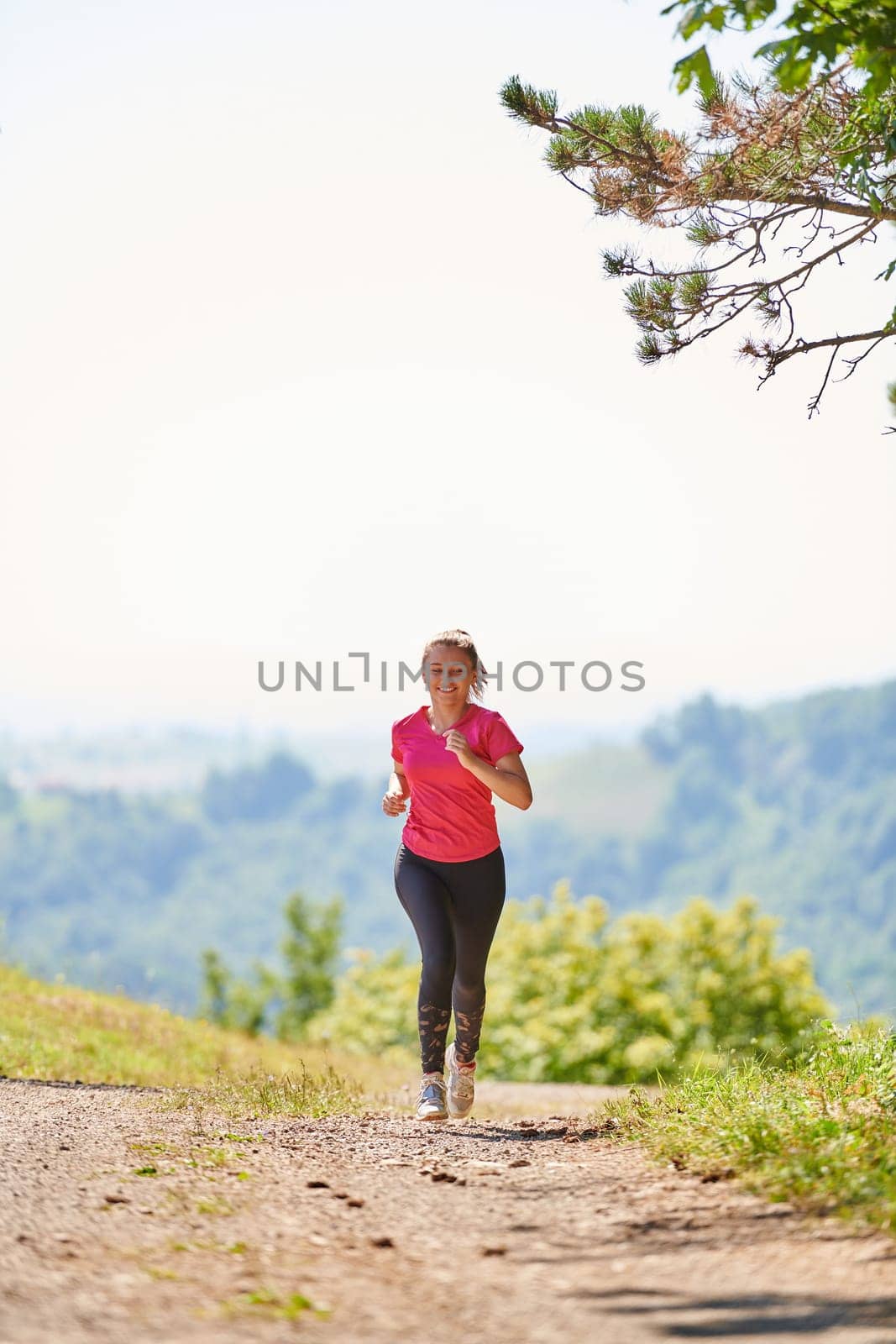 woman enjoying in a healthy lifestyle while jogging on a country road through the beautiful sunny forest, exercise and fitness concept