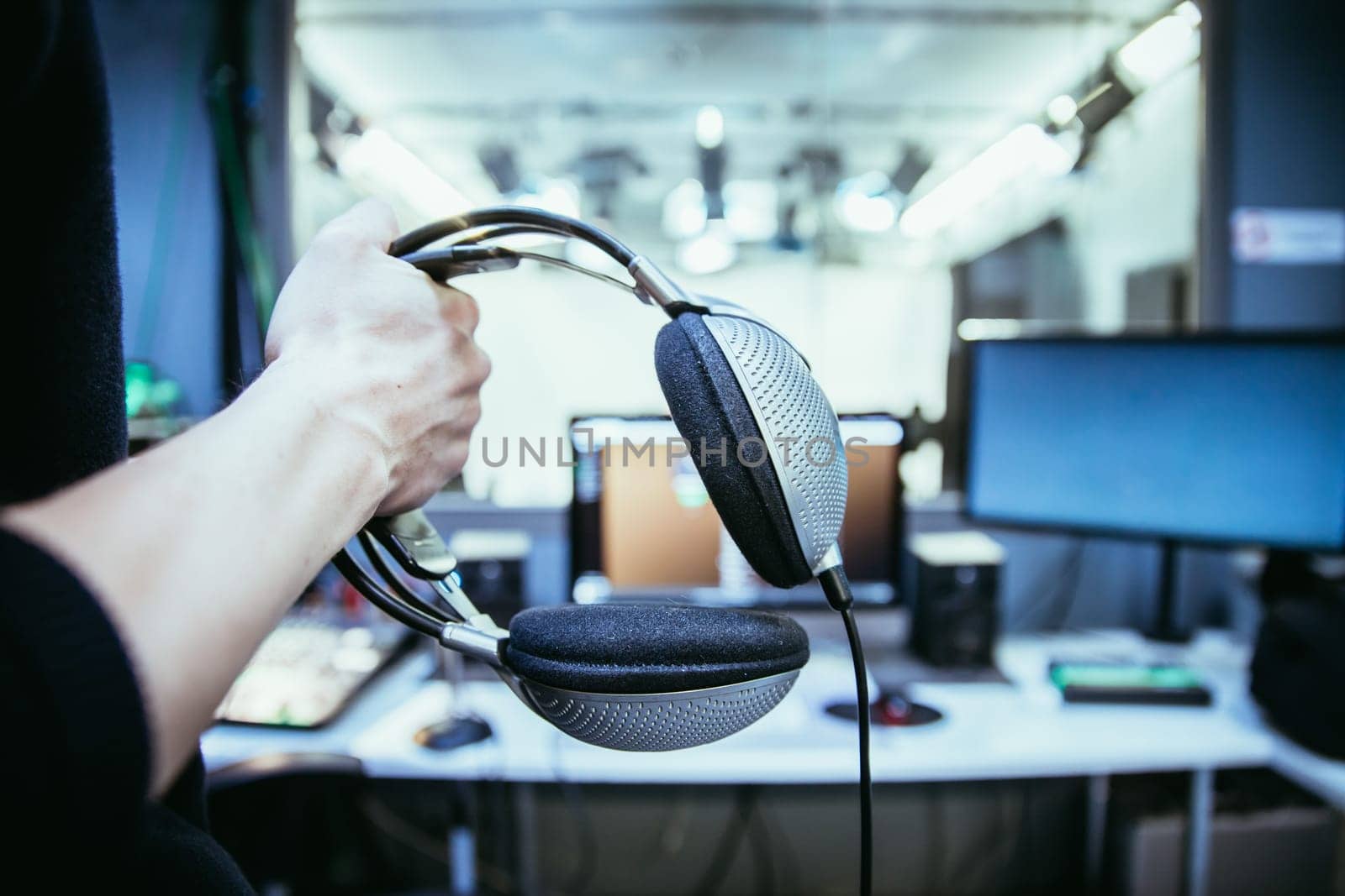 Young man holds headphones in the recording studio. Buttons, studio, screens and equipment in the blurry background