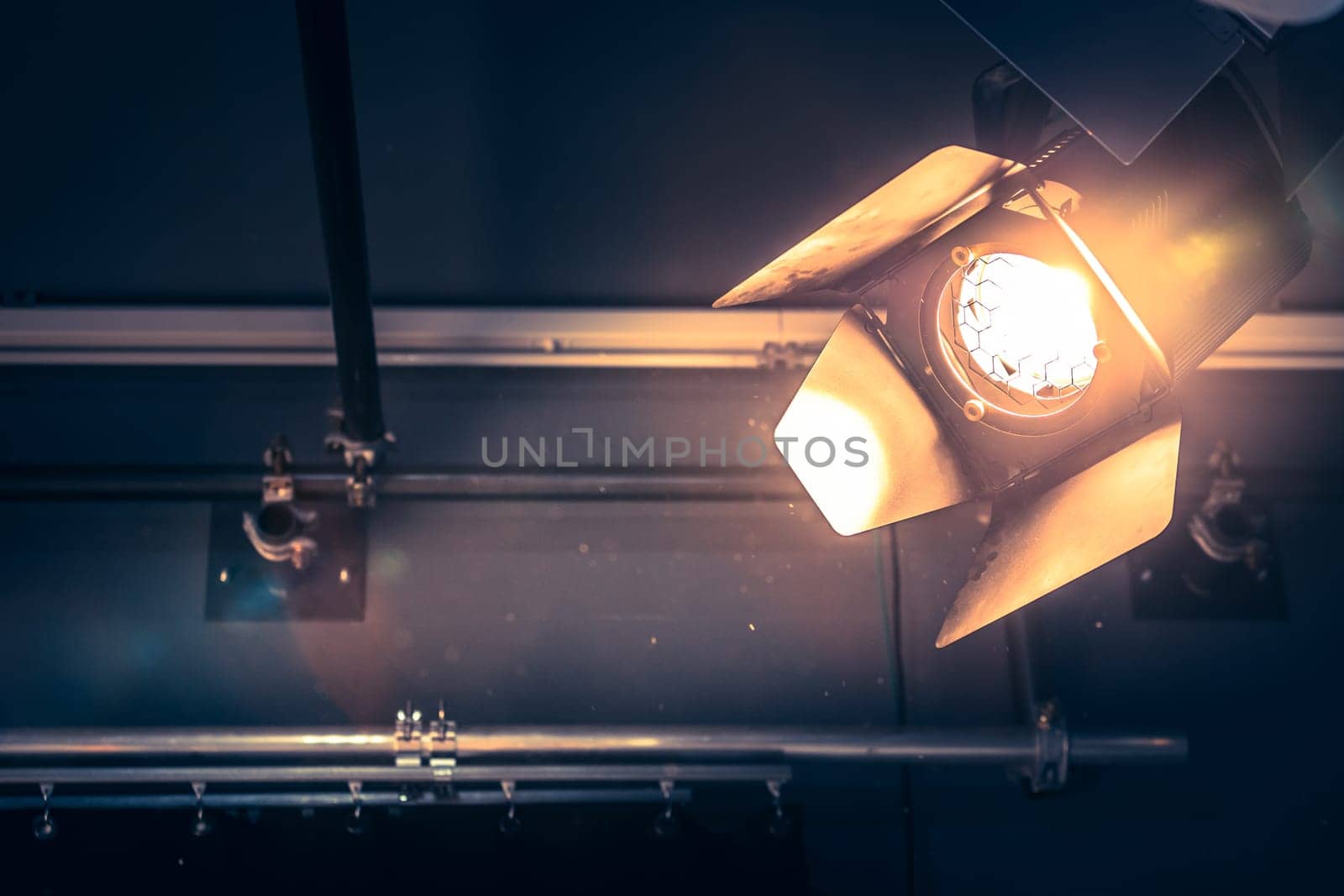 Professional orange studio spotlight hanging on the ceiling. Lighted dust particles and lens flares.