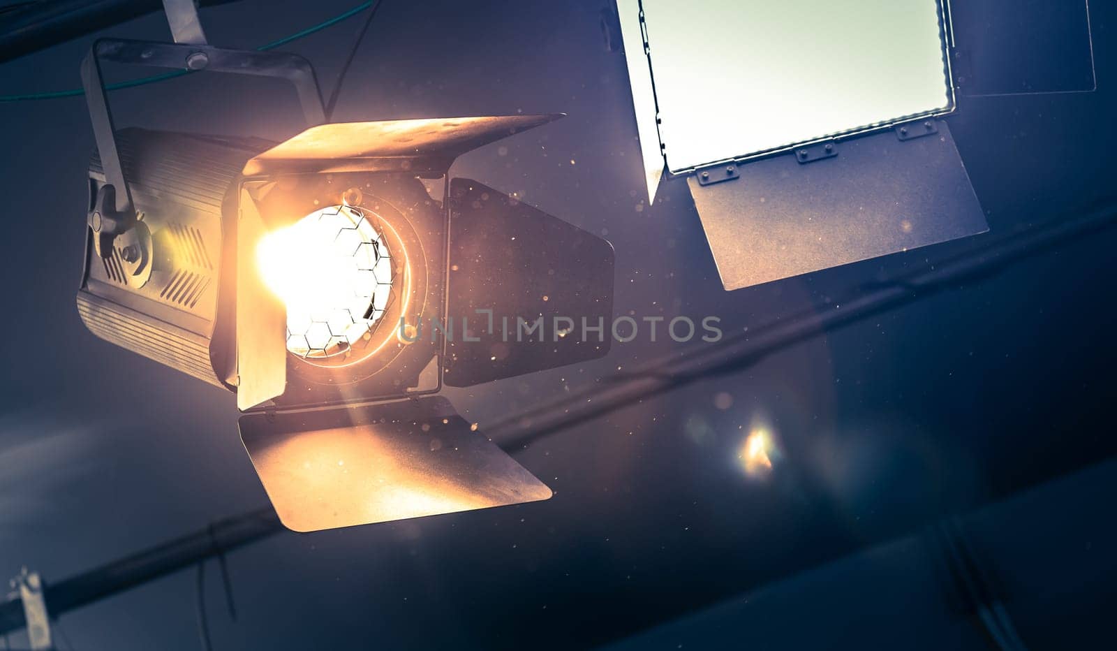 Professional orange studio spotlight hanging on the ceiling. Lighted dust particles and lens flares.