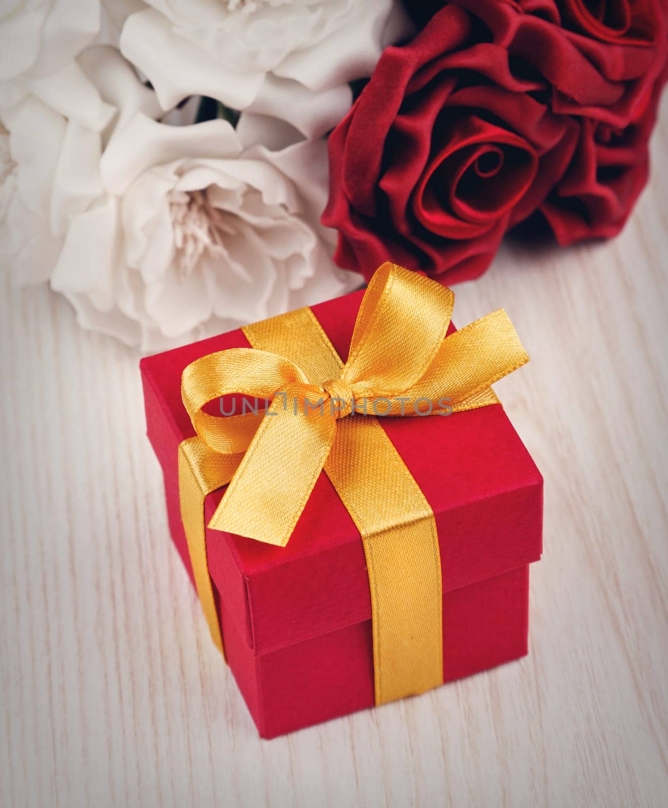 red and white roses and red gift box with yellow ribbon on wooden surface