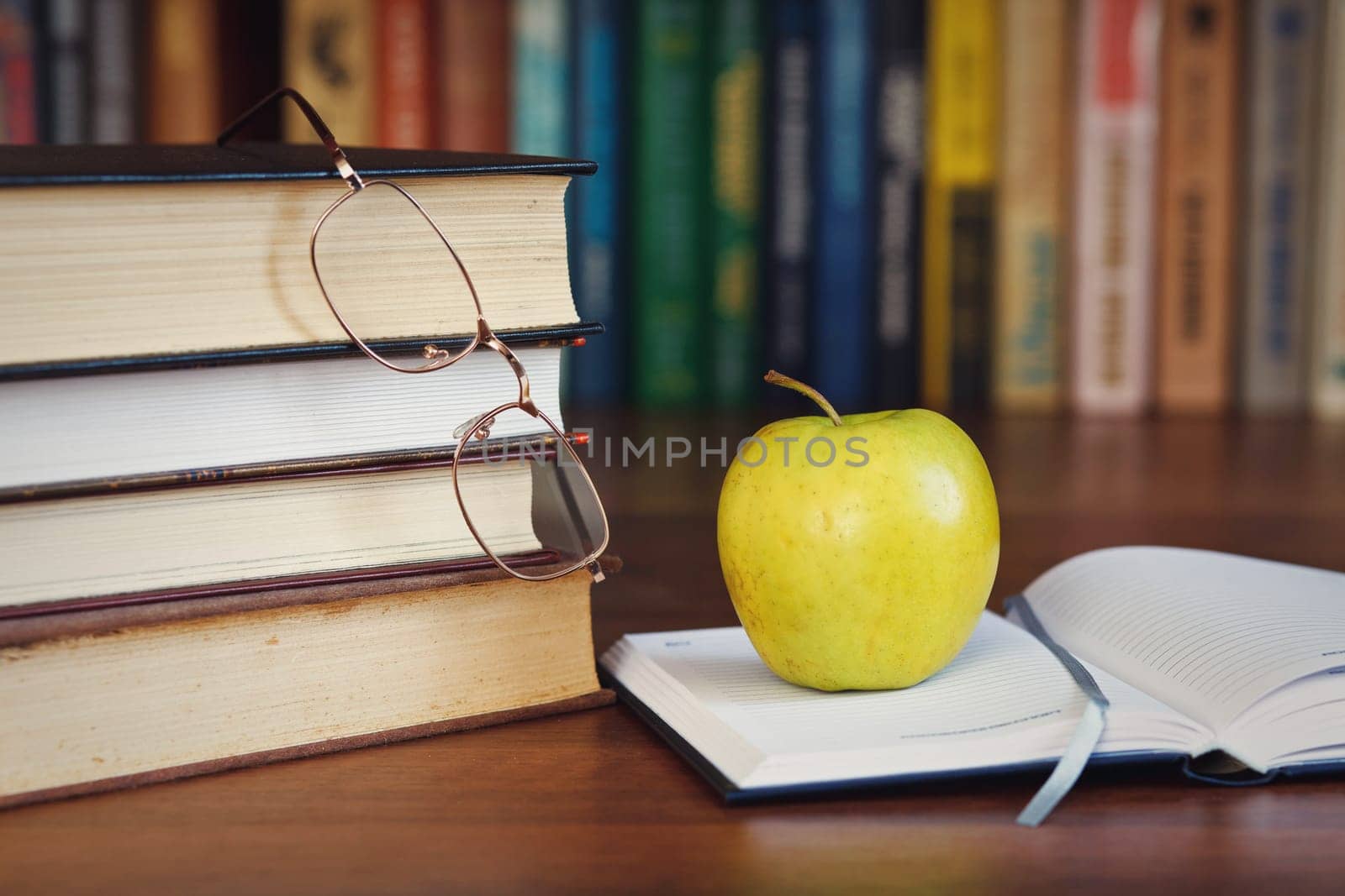 green apple on the open book with books and glasses